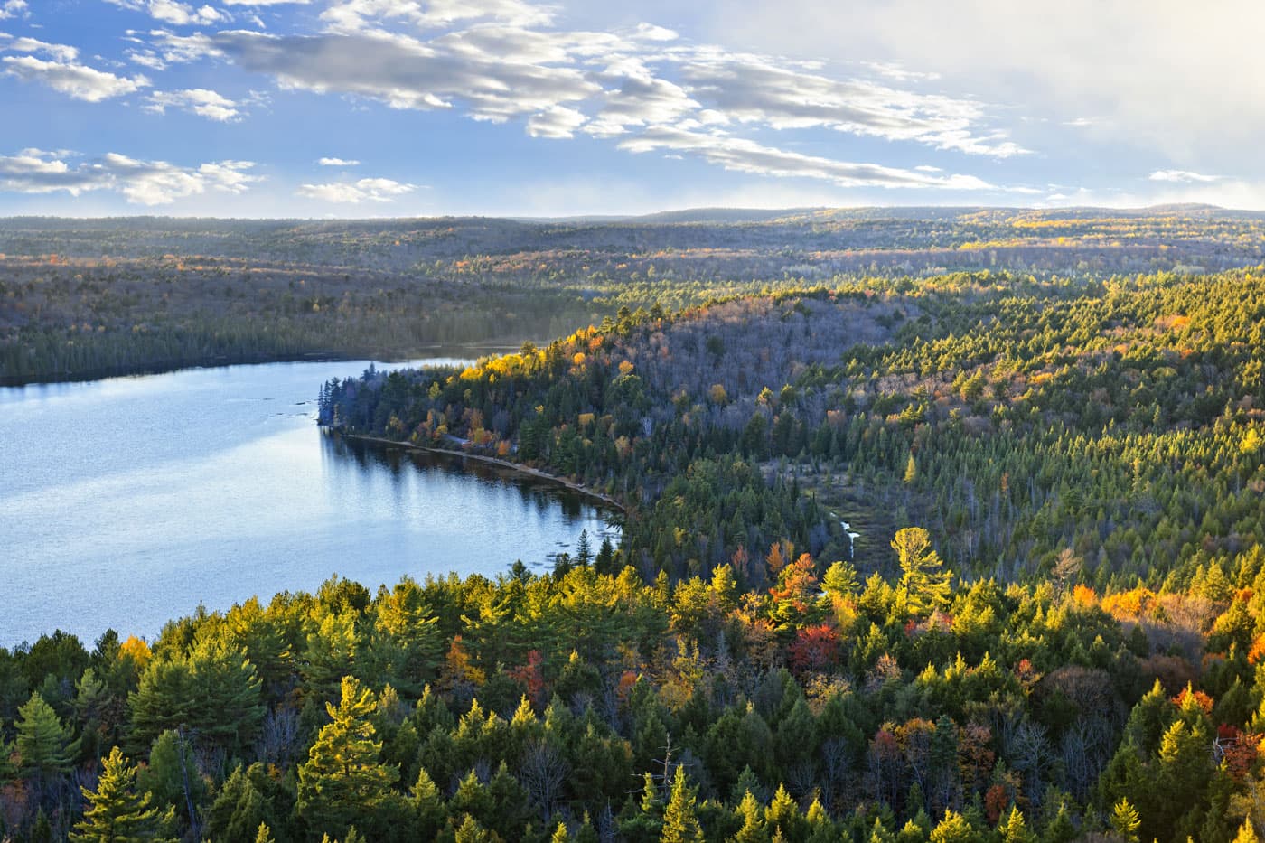 A lake winding between hills in Algonquin with the first orange and yellow showing in the forest