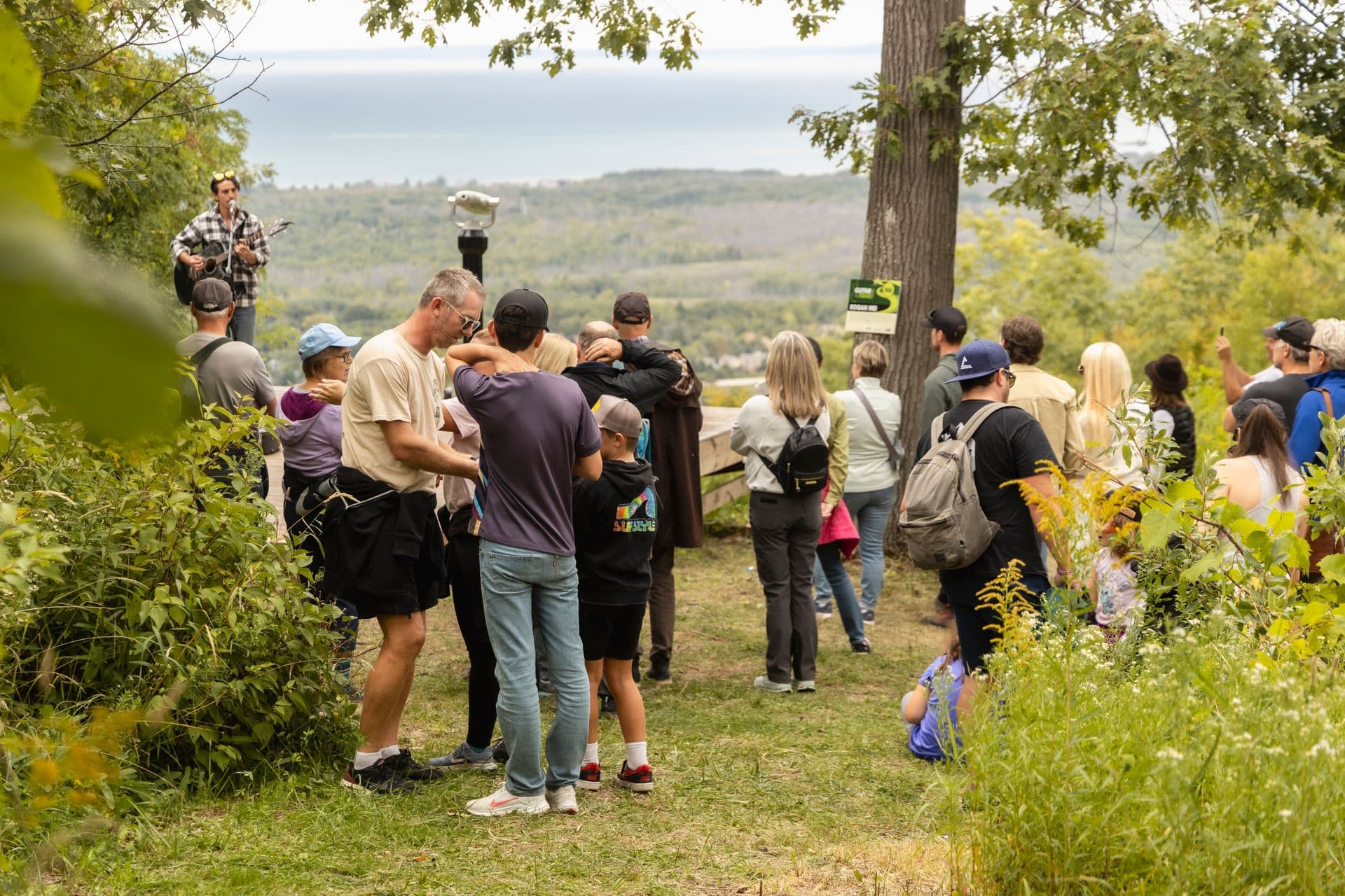 A crowd gathered round a performer on a grassy clifftop above Georgian Bay at the Guitar Trail festival
