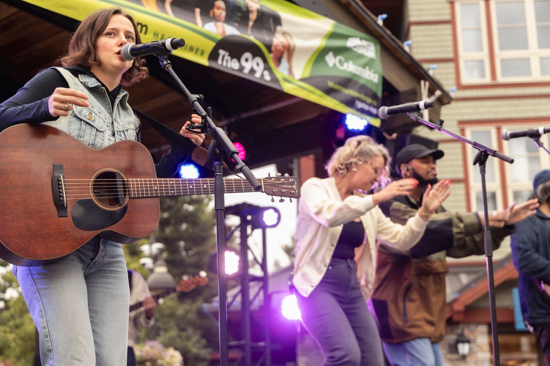 A singer with a guitar on the village stage with the crowd's hands up in front