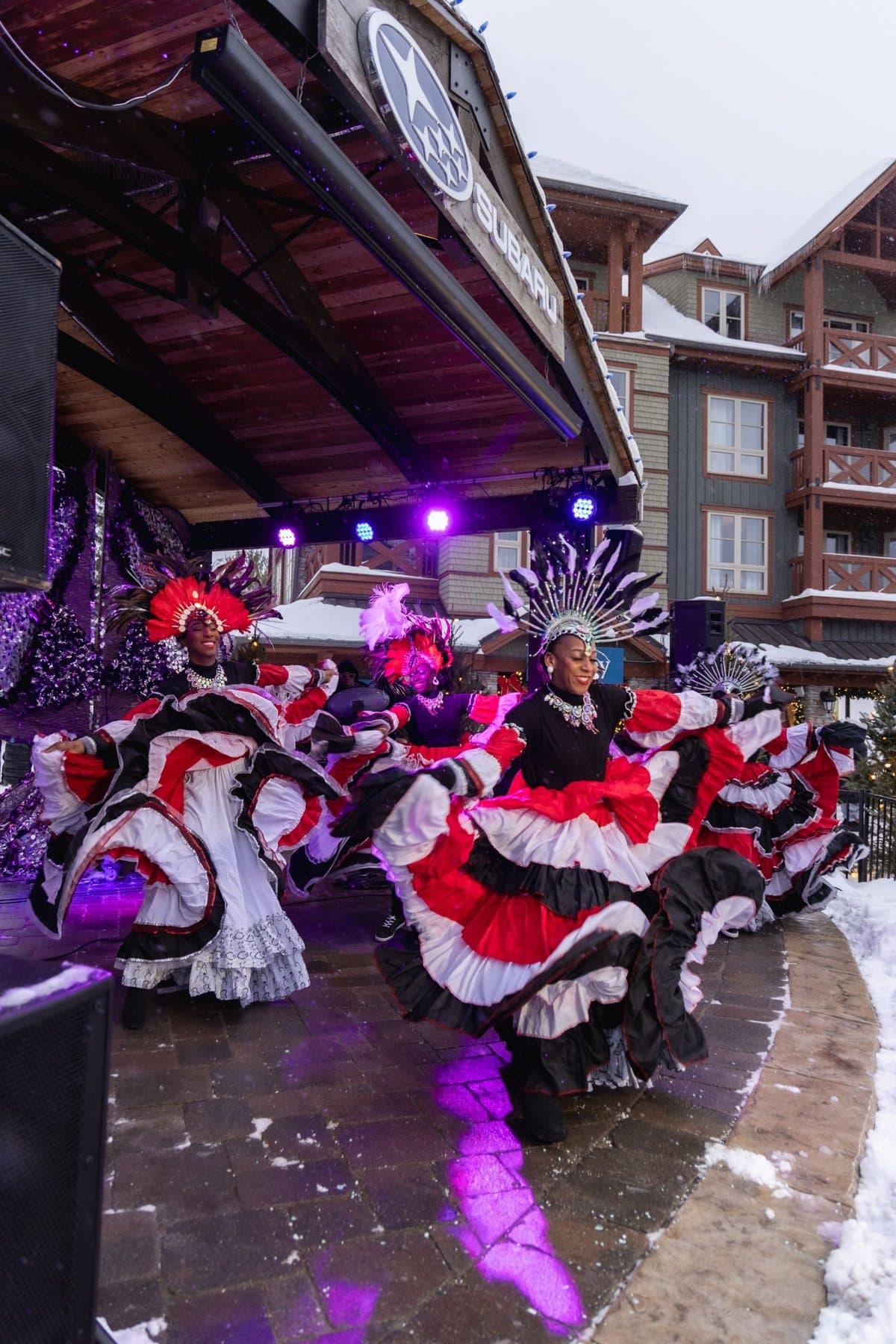 Dancers in red, black and white ruffled skirts and feathered headdresses performing on the outdoor stage in the snow