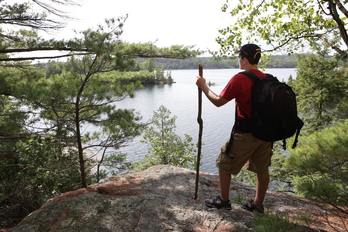 A hiker with a walking stick standing on granite above the lake, backpack on