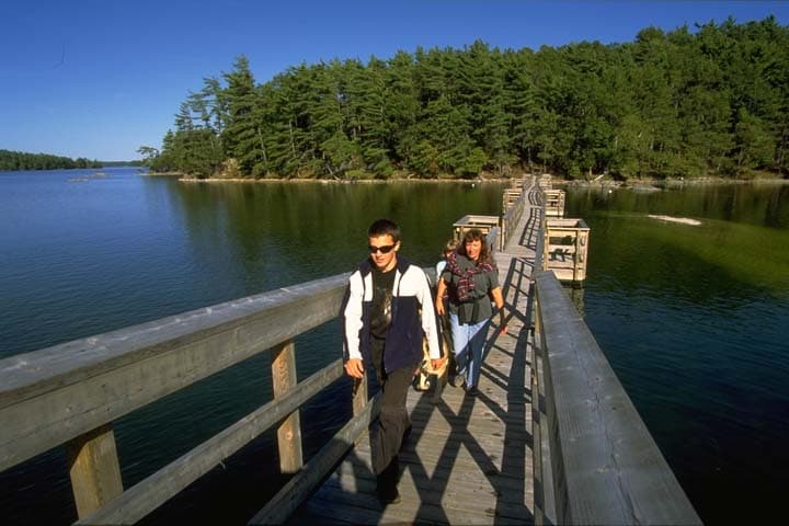 Two people walking a low wooden bridge across the water between wooded shores