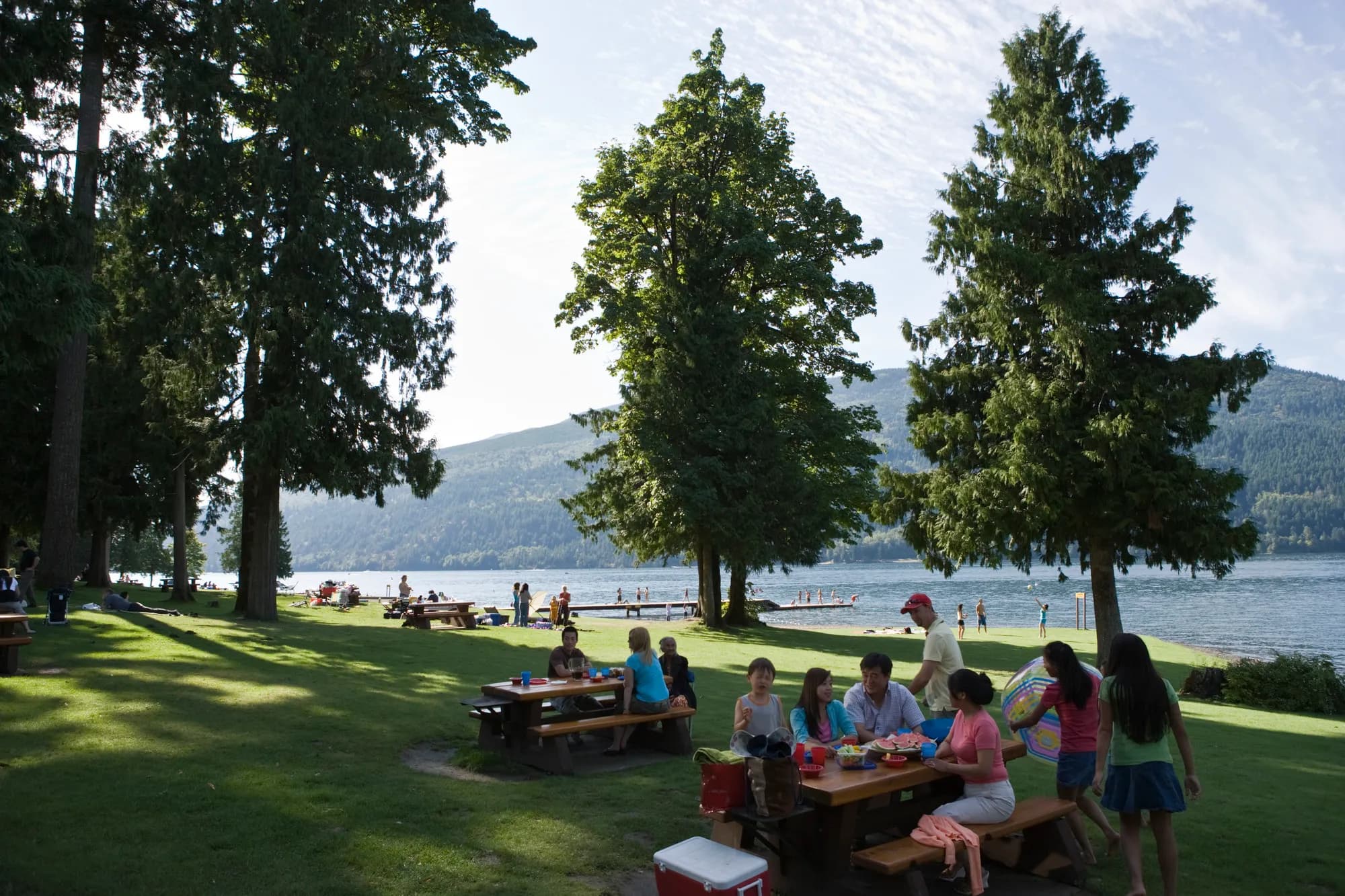 The grassy day use area at Maple Bay, with picnic tables, swimmers and the mountains behind