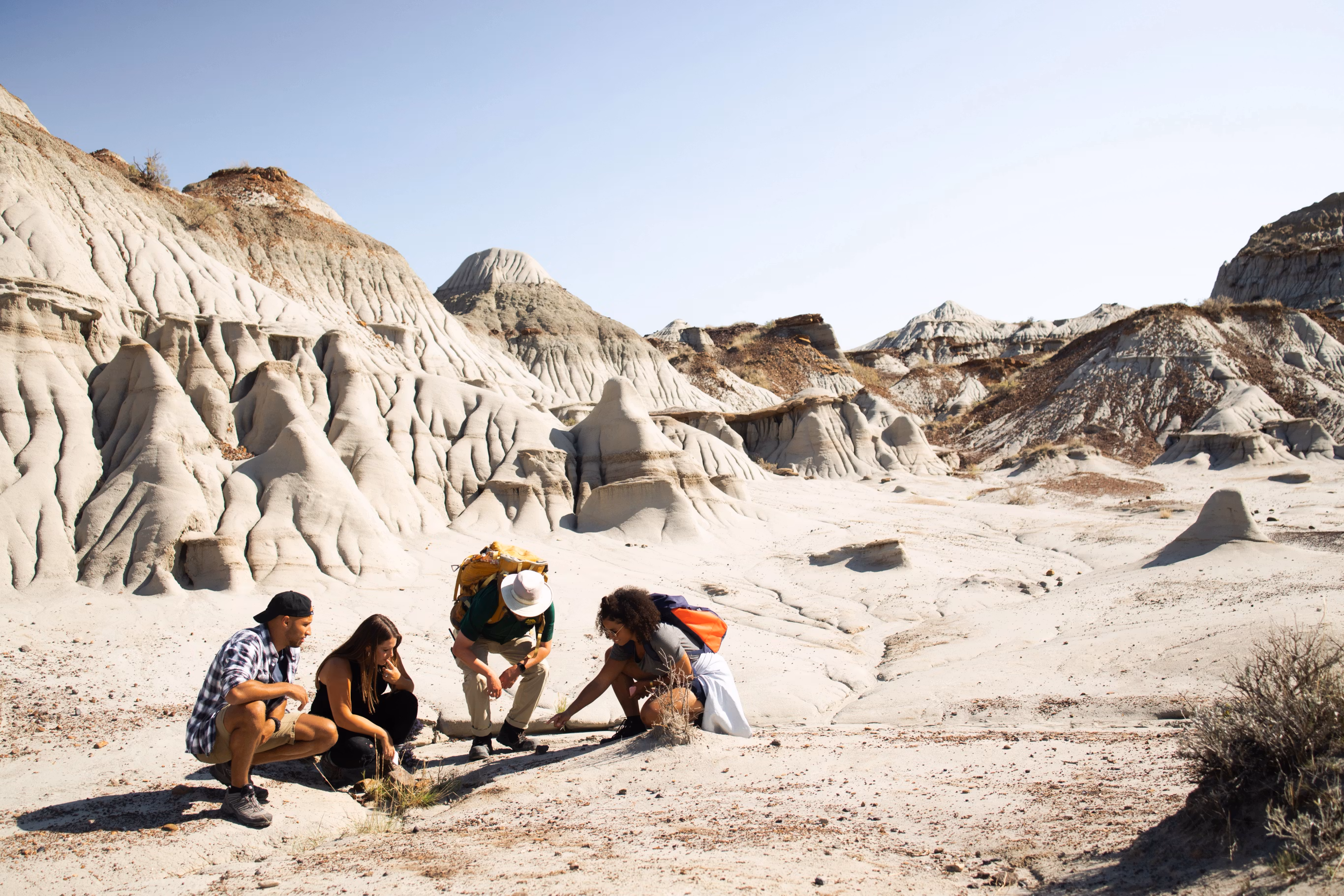 Visitors crouched on the badlands floor with hoodoos rising behind them at Dinosaur Provincial Park