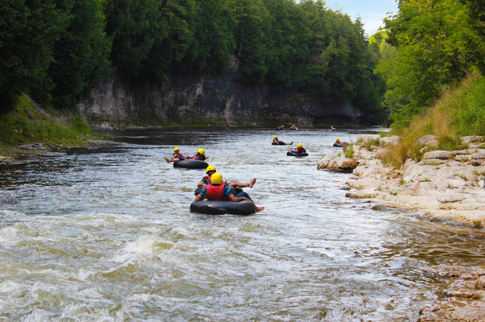 Tubers in helmets floating the rapids of the Grand River below the gorge walls