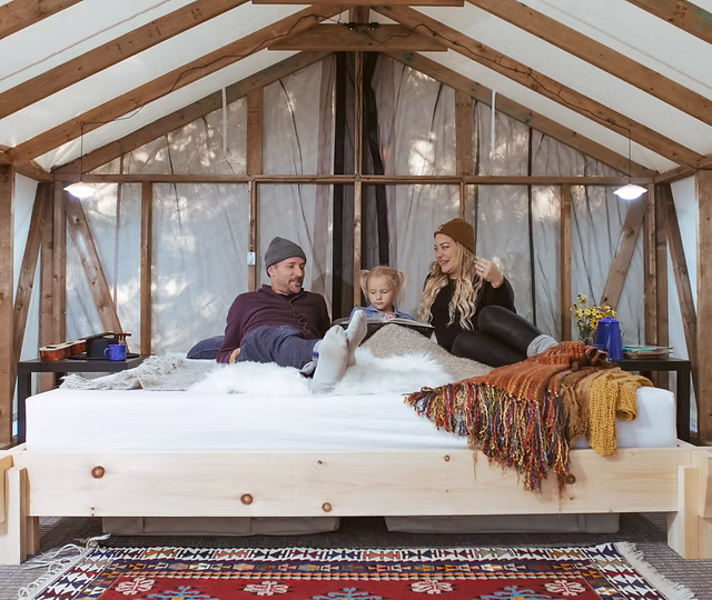 A family reading in bed inside a canvas-walled cabin at Four Corners Algonquin