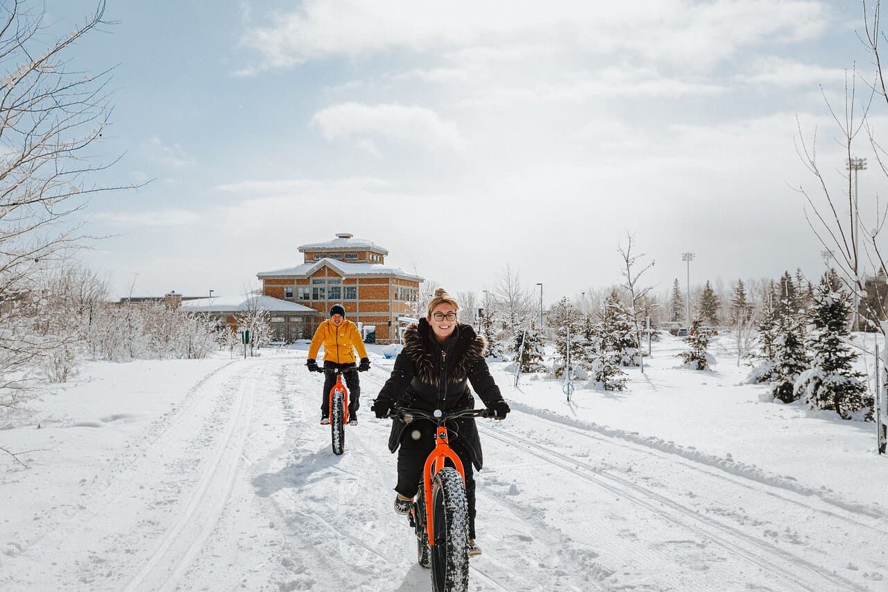 Two fat bikers riding a packed snow trail past the lodge at Gatineau Park
