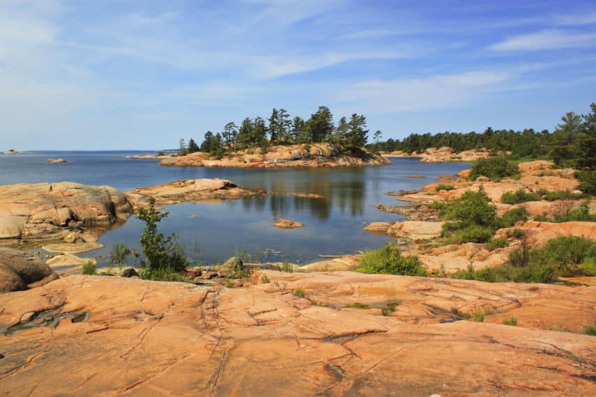 Pink granite shelving into calm water, with a pine covered island across the channel