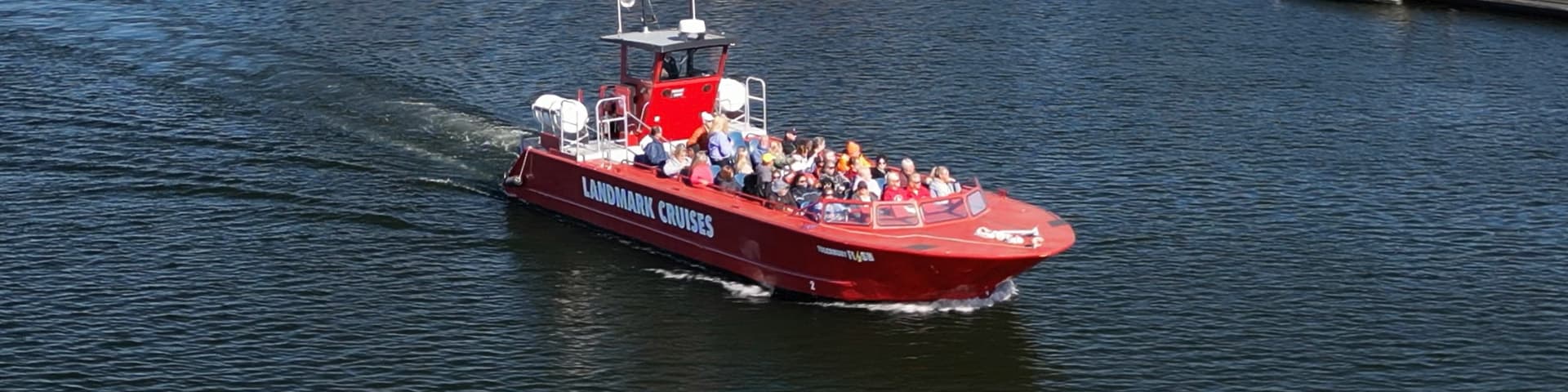 The red Landmark Cruises boat running across open water with a full deck of passengers