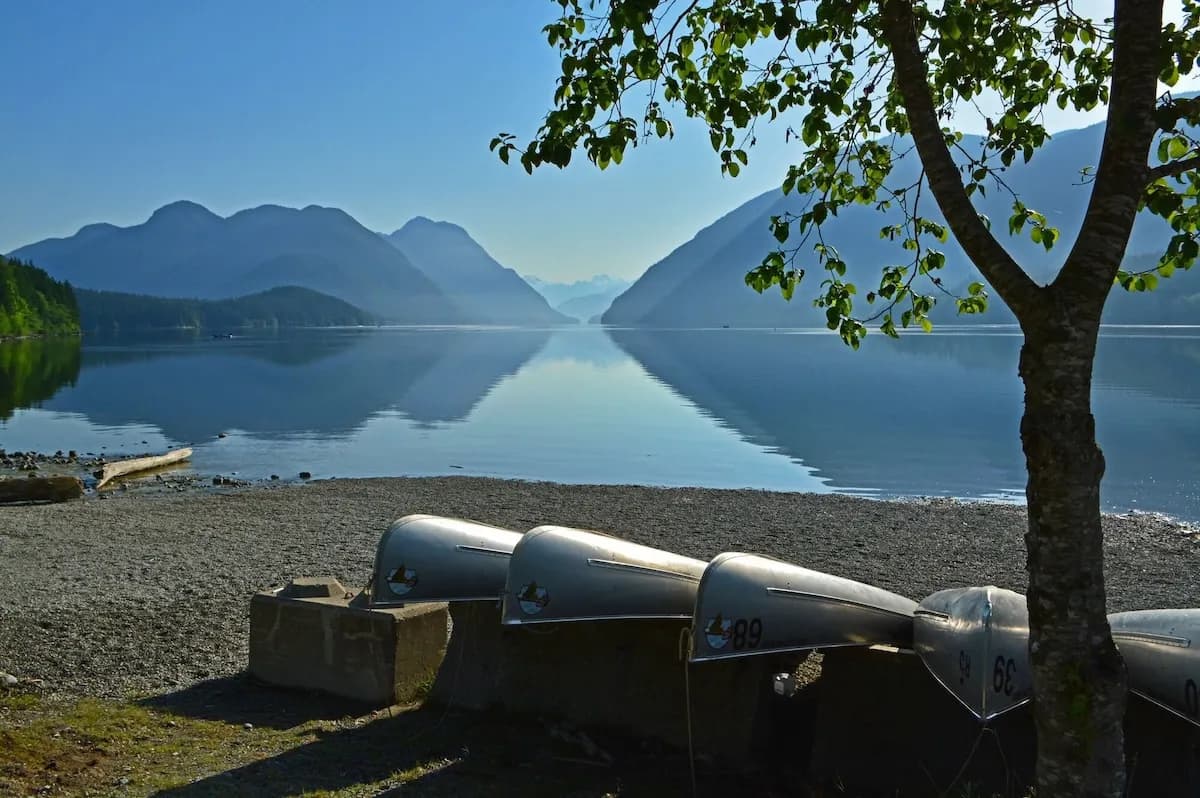 Canoes pulled up on the beach at Alouette Lake with the mountains reflected in the water