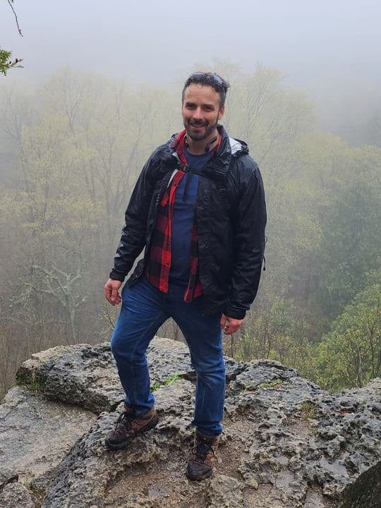 Jeff, a Parkbus guide, standing on a rock lookout above a misty forest, smiling at the camera