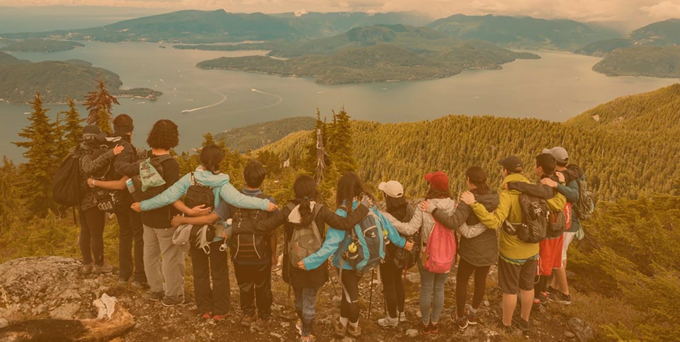 A Parkbus group standing arm in arm on a mountain lookout, looking out over islands and water far below