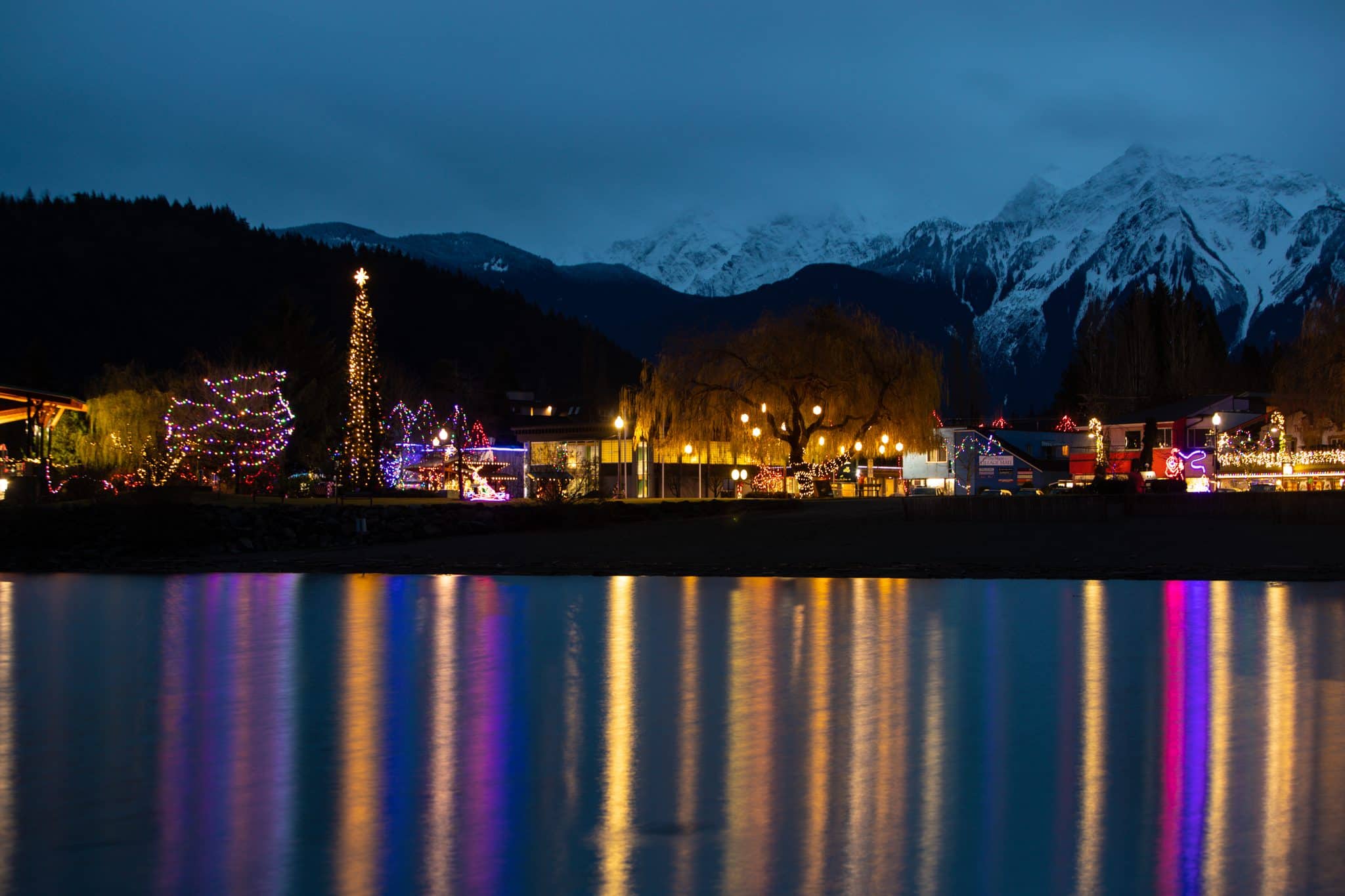 Harrison Hot Springs at night during Lights by the Lake, coloured lights along the shore reflected down the water with snowy mountains behind