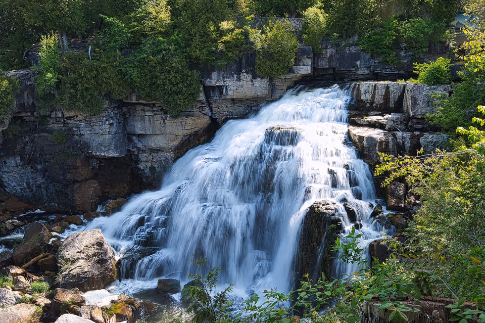 Inglis Falls in long exposure, white water sliding over layered limestone into the gorge