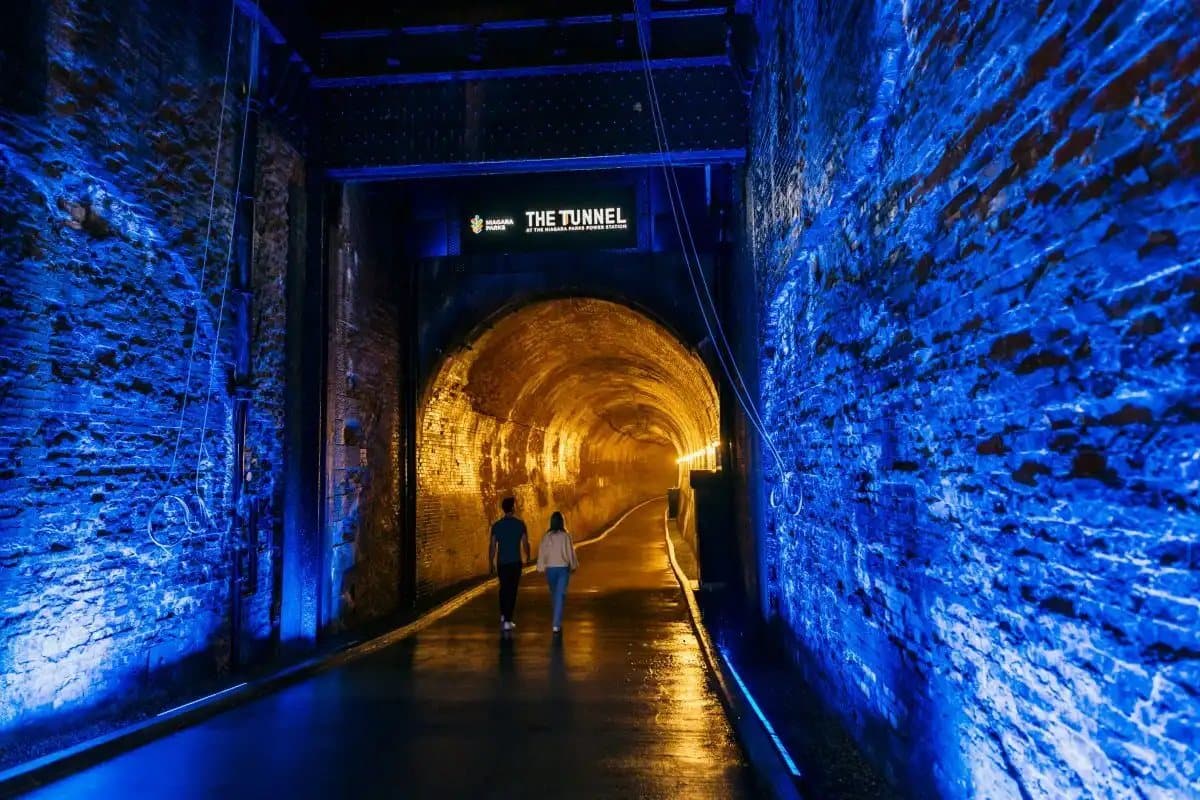 The entrance to the Tunnel at the Niagara Parks Power Station, brick walls lit blue and the tunnel glowing gold ahead