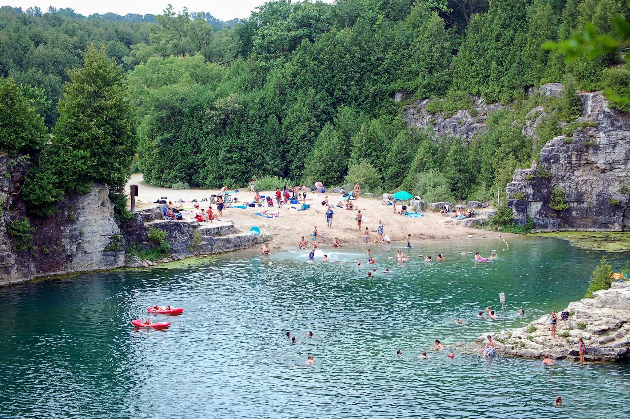 The turquoise water and busy sand beach at Elora Quarry from the cliffs above