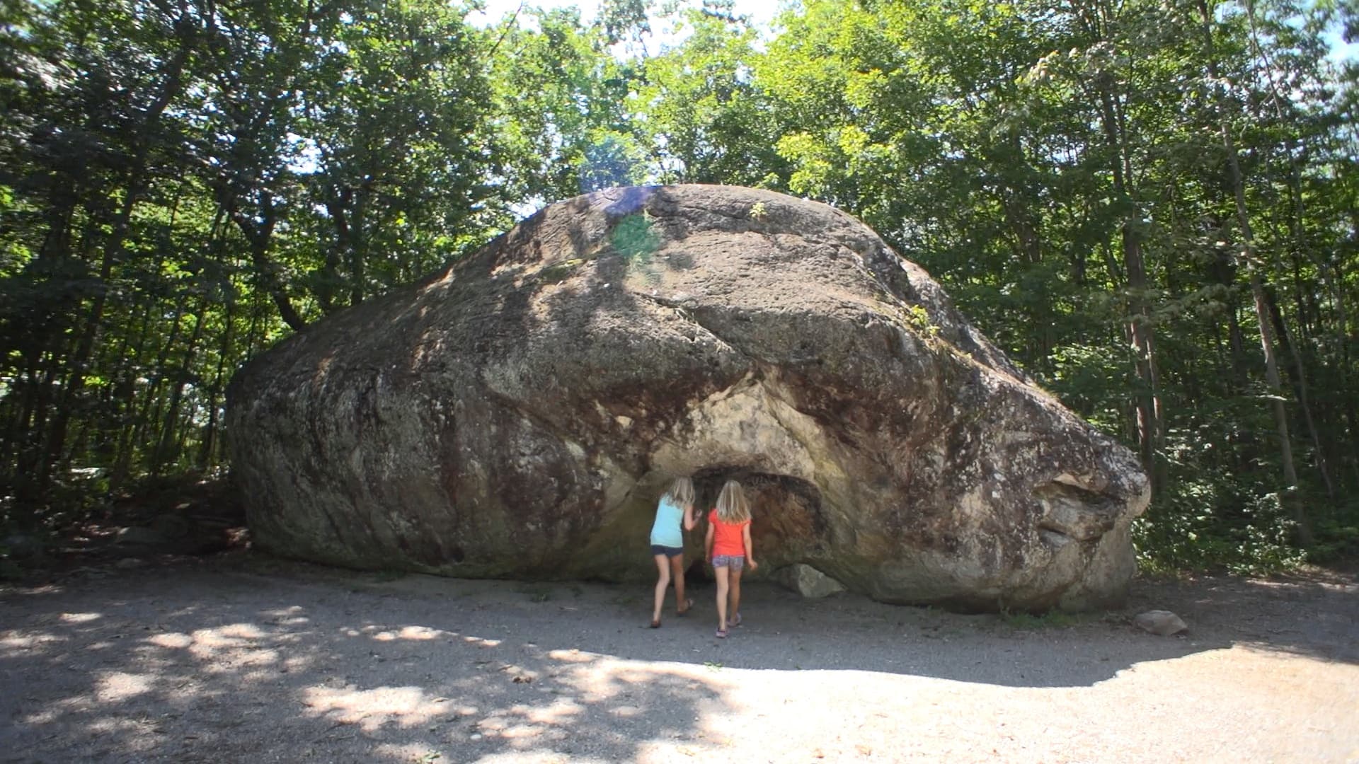 Two children standing beside the Bleasdell Boulder, a huge glacial erratic in the forest