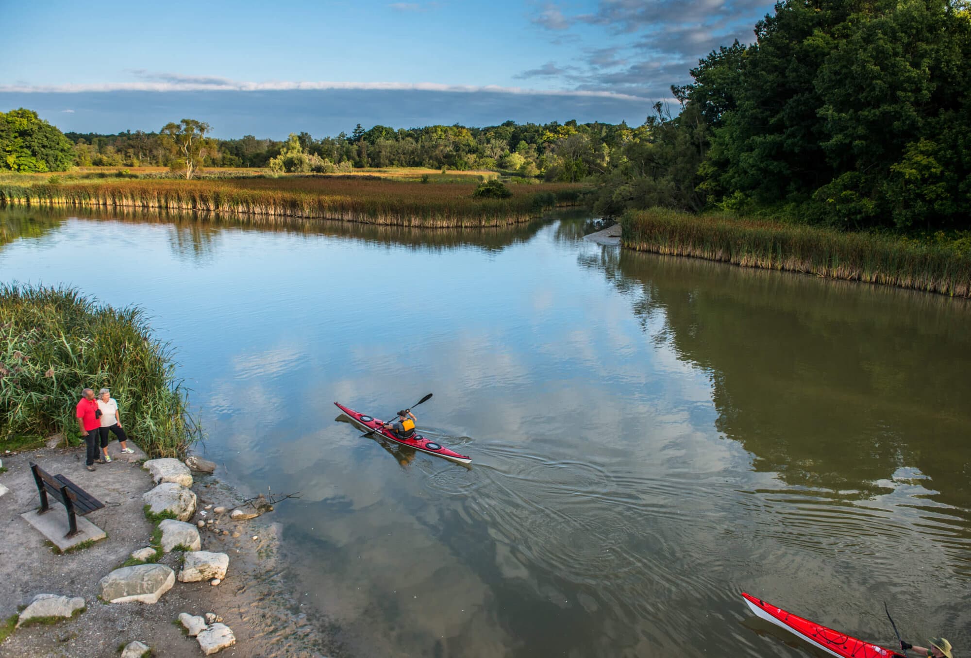A kayaker on the still water of the Rouge marsh with a red kayak pulled up on the shore