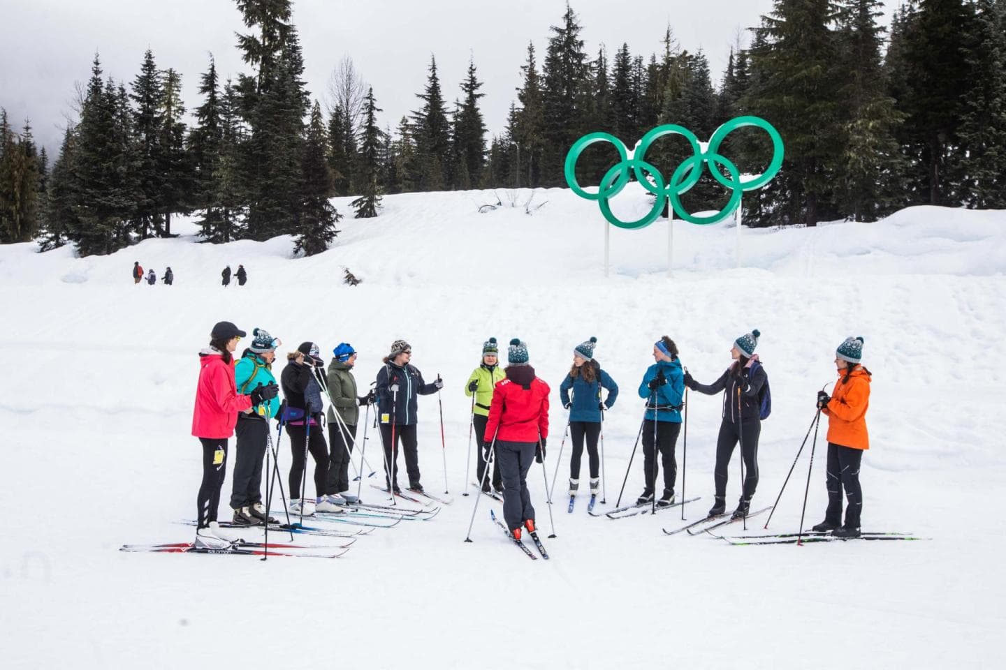 A group of skiers standing on the snow beneath the Olympic rings