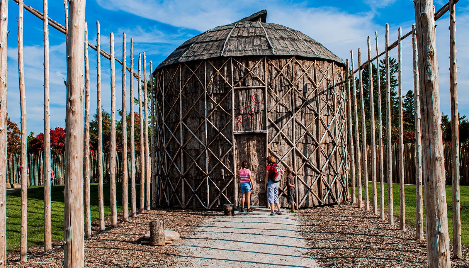 A reconstructed bark-walled longhouse behind a tall wooden palisade
