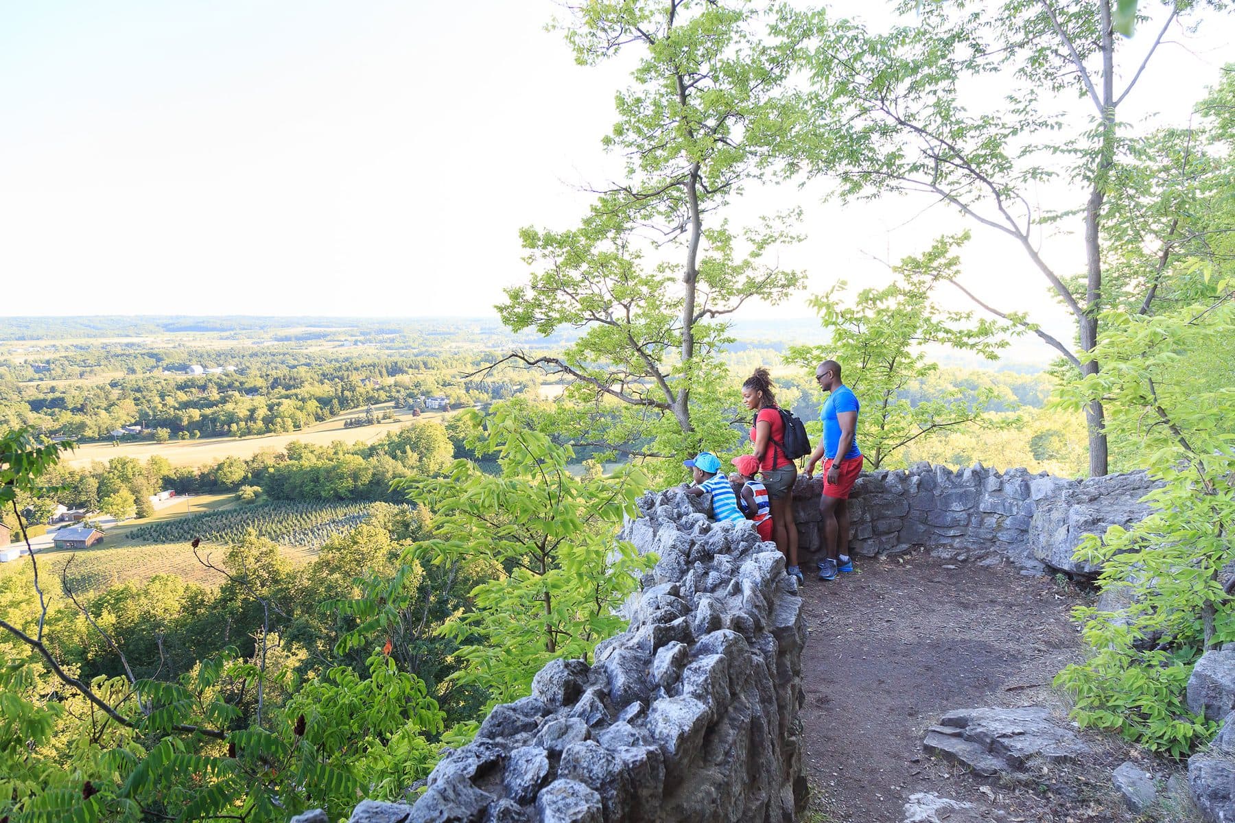 Two hikers standing at a stone-walled lookout above a wide green valley