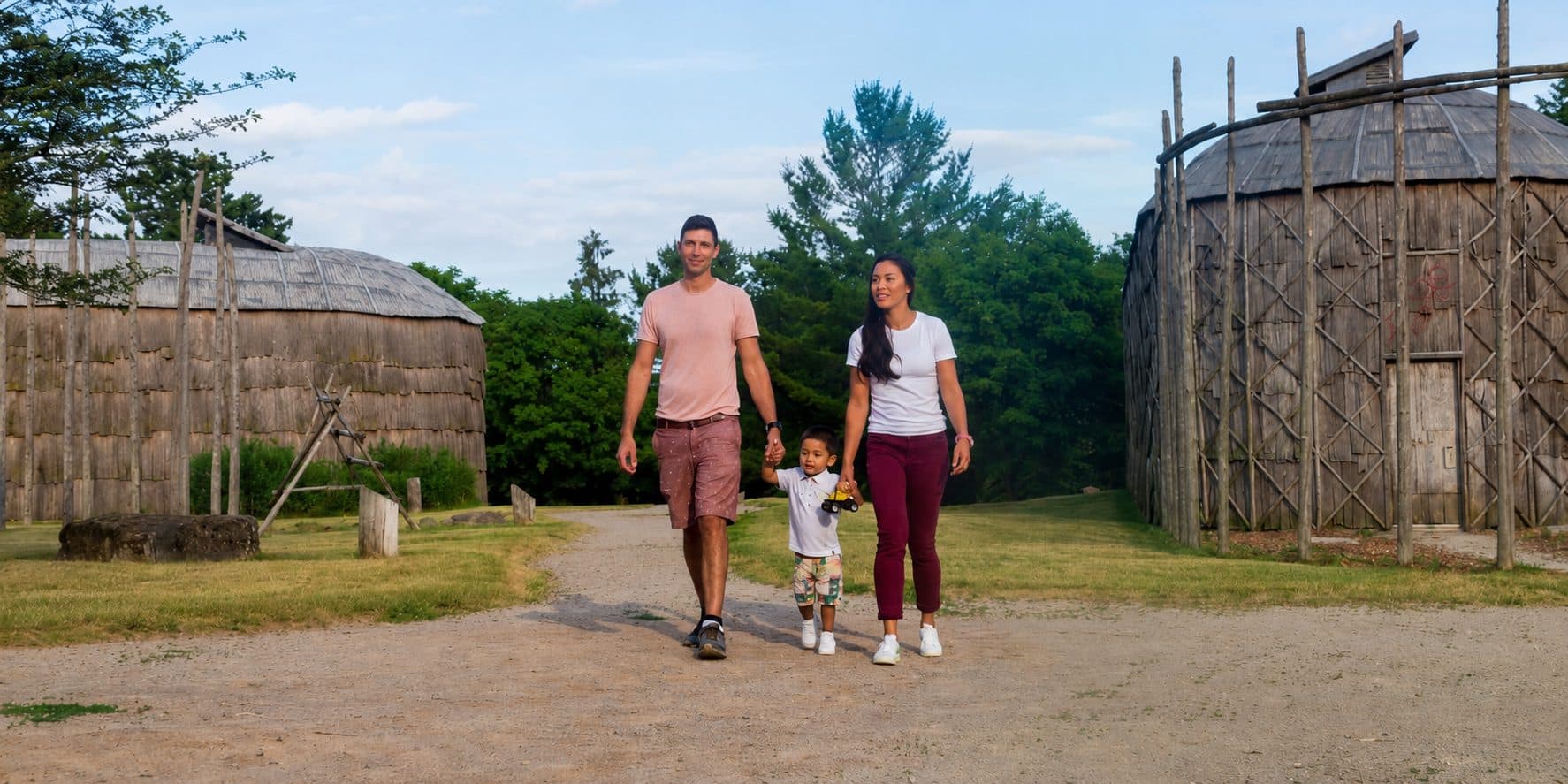A family walking the path between two reconstructed bark-walled longhouses