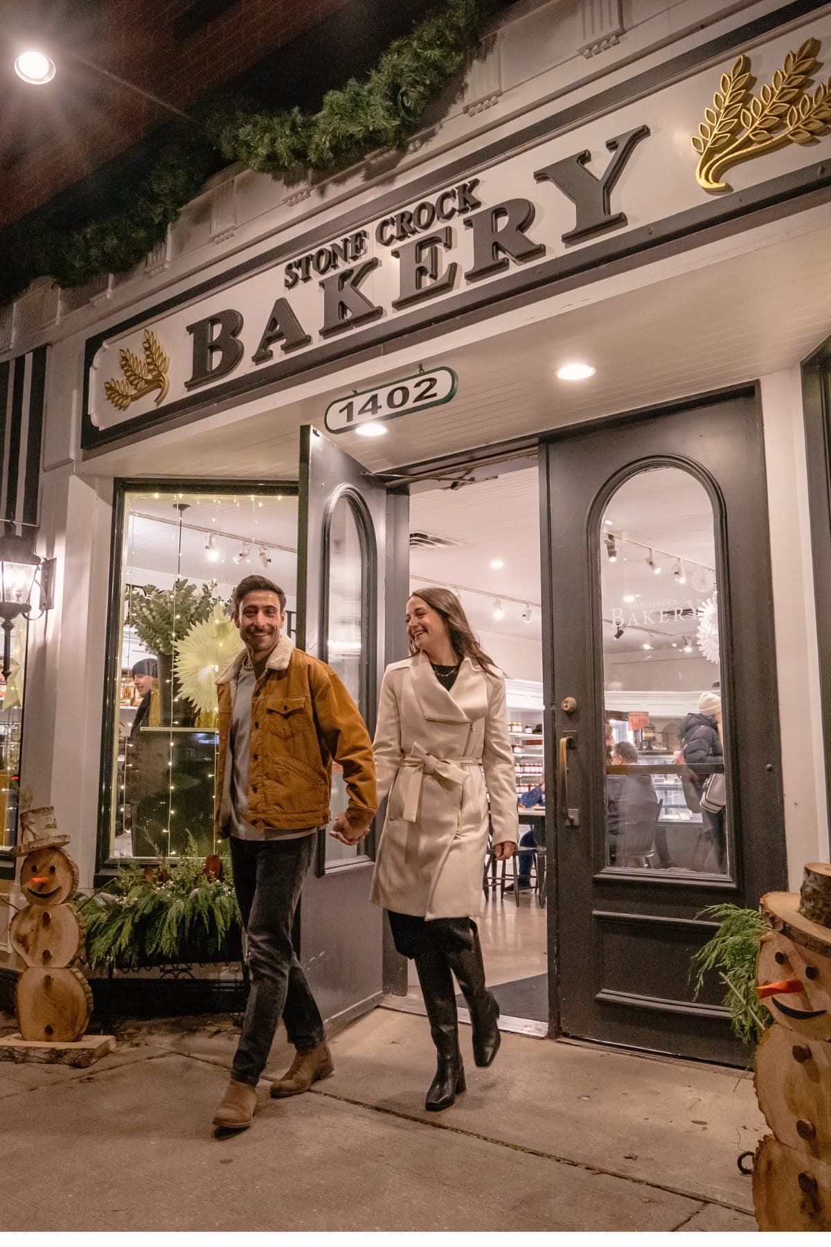Two people leaving the Stone Crock Bakery in St. Jacobs, the shop front dressed with greenery and lights