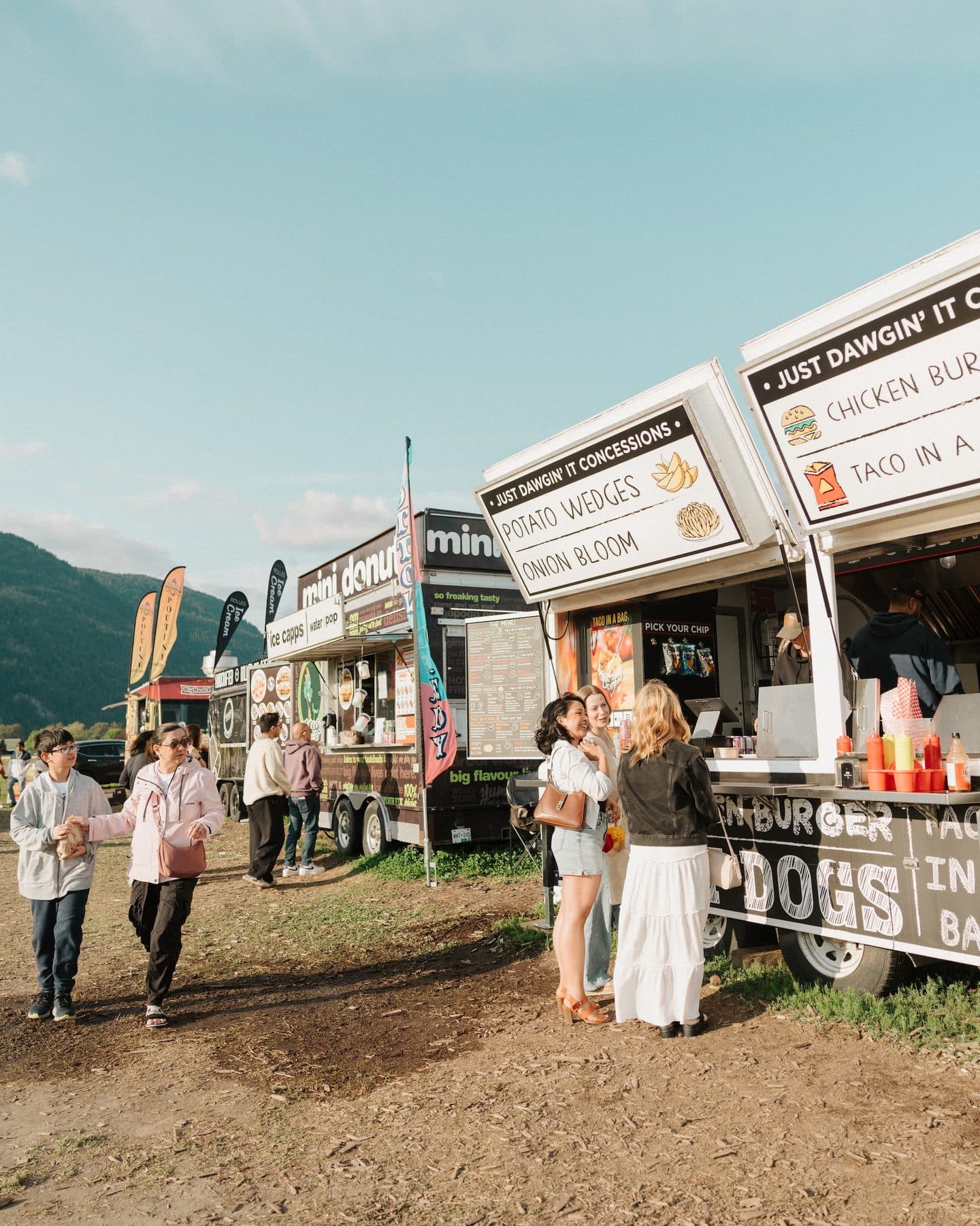 Food trucks parked at the edge of the festival with visitors queueing in the sun