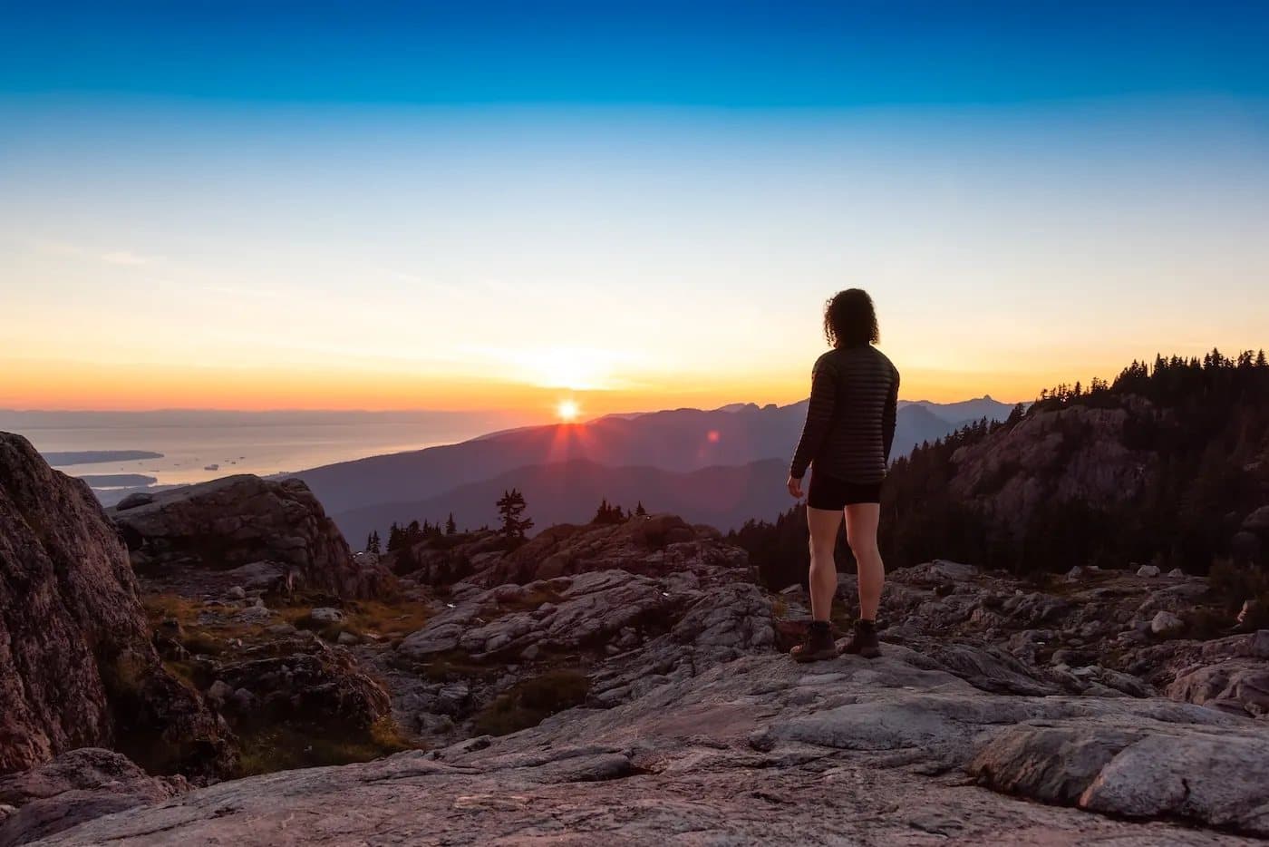 A hiker watching the sun come up over the water from Mount Seymour