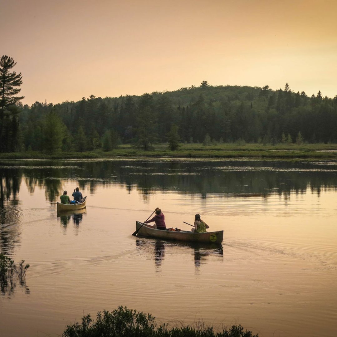 Two canoes on calm water at sunset, with forested hills behind