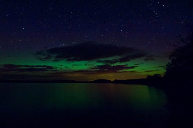 A faint green aurora low over a dark lake under a starry sky