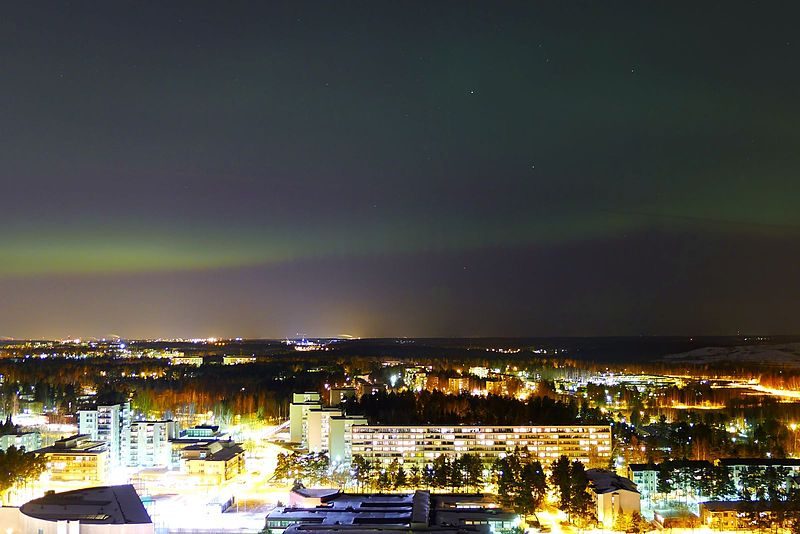 Green northern lights in the sky above the lights of a city