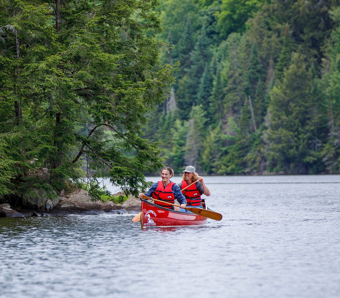 Two people paddling a red canoe on a lake with forest behind them