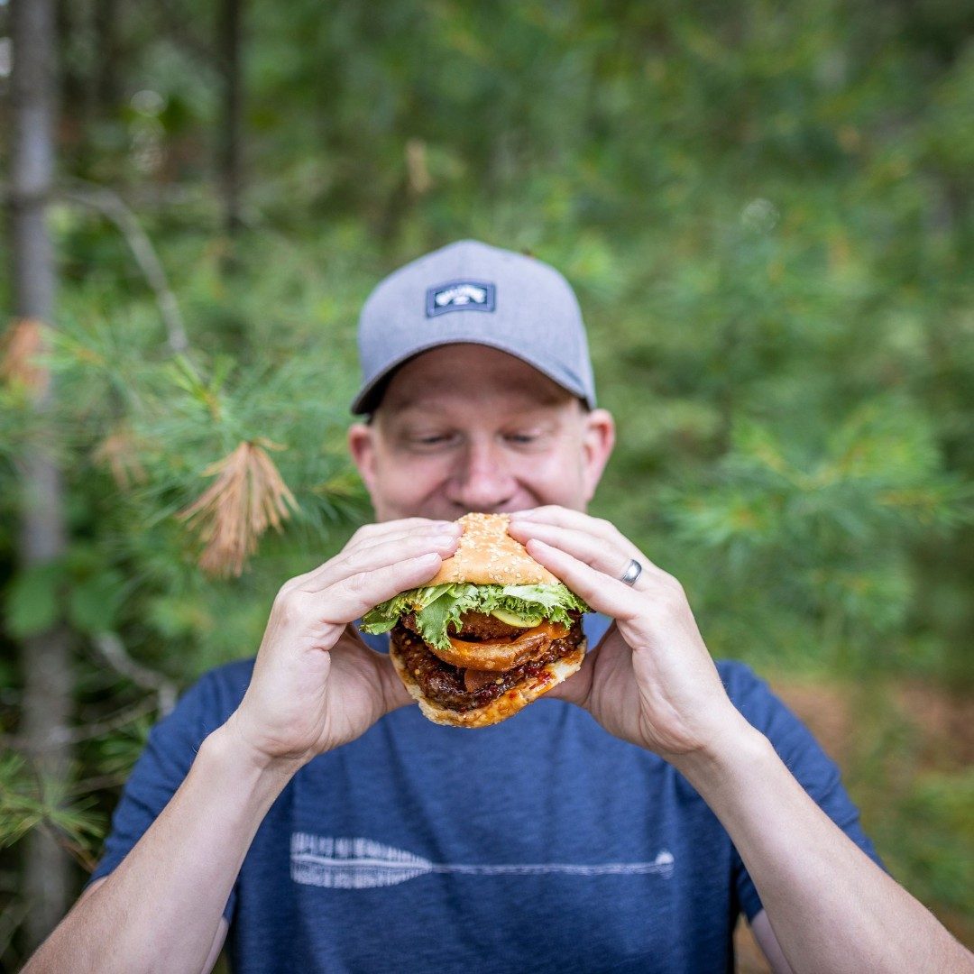 A man in a cap eating a burger outdoors
