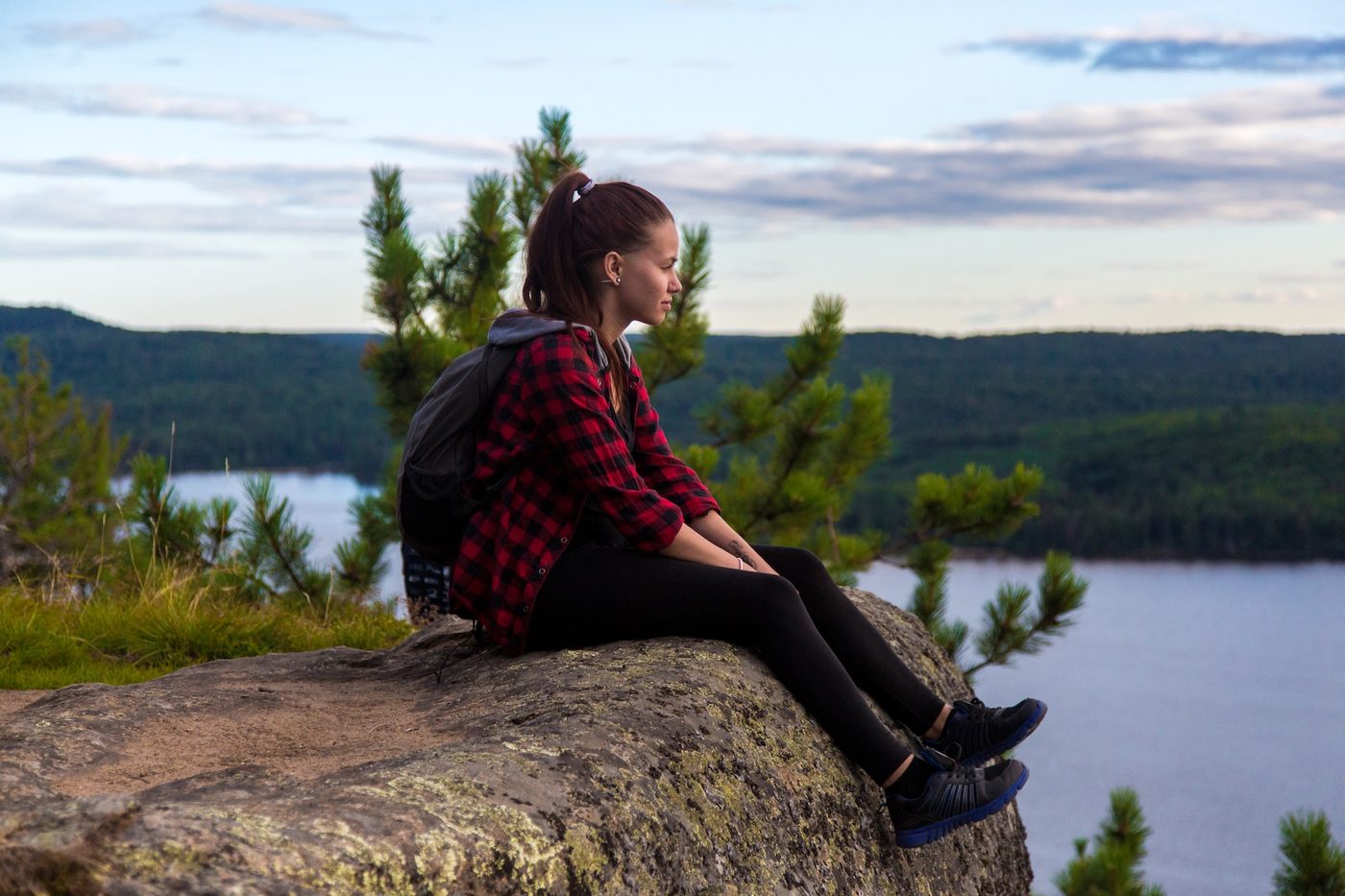 A hiker sitting on a rock at a lookout, above a lake and miles of forest