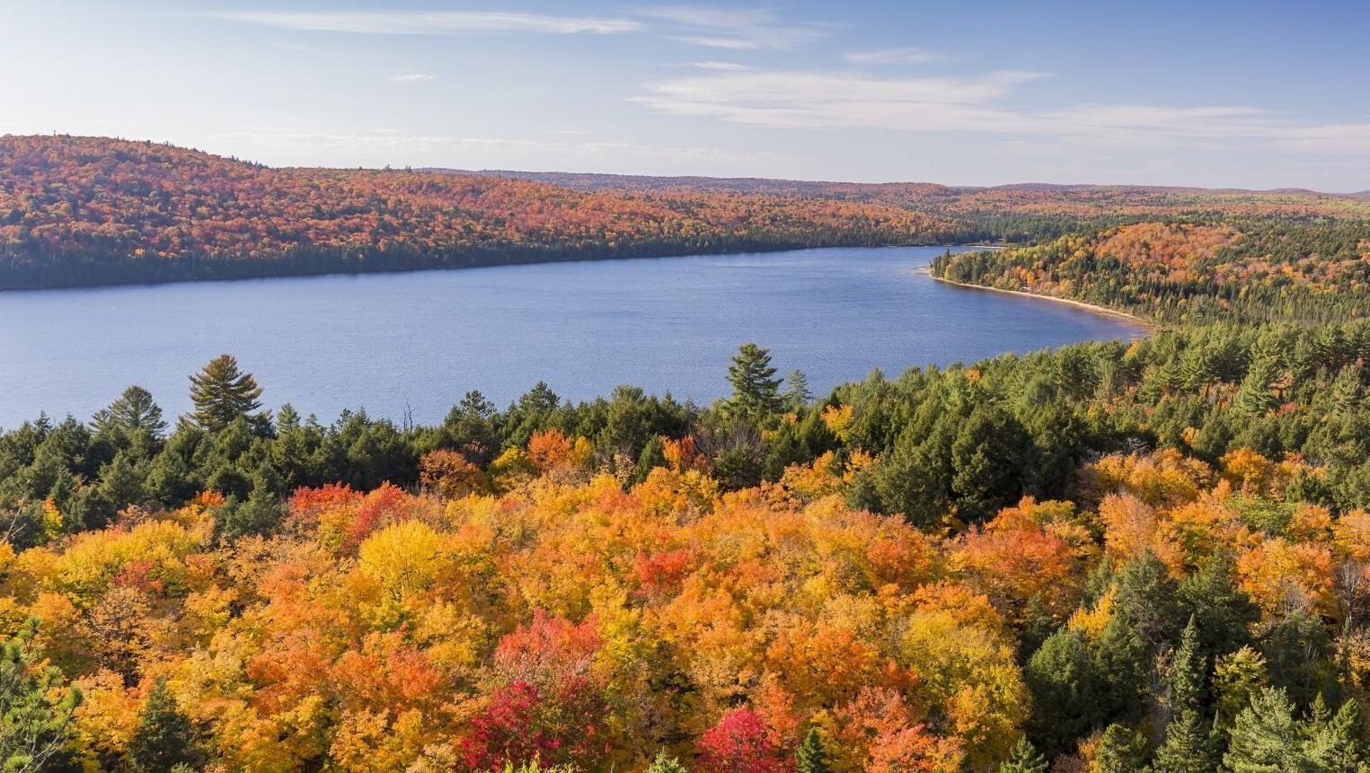 A blue lake below hills of red, orange and gold forest