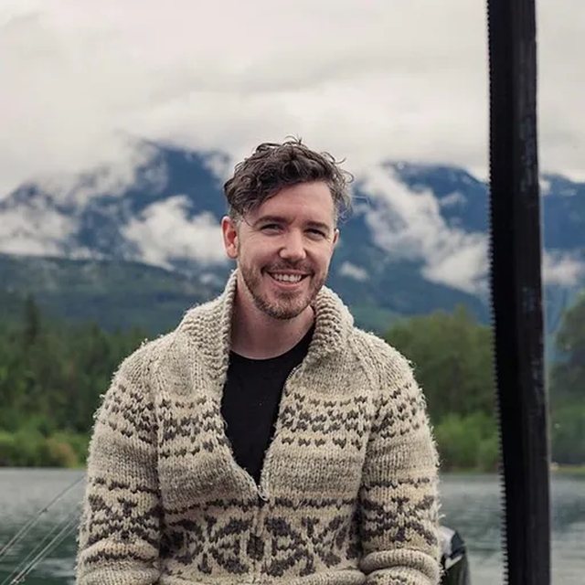 Matthew Hardy Thomas outdoors, with mountains and water behind him