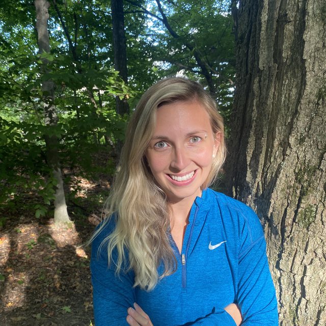Rebecca Koroll standing beside a large tree in the woods
